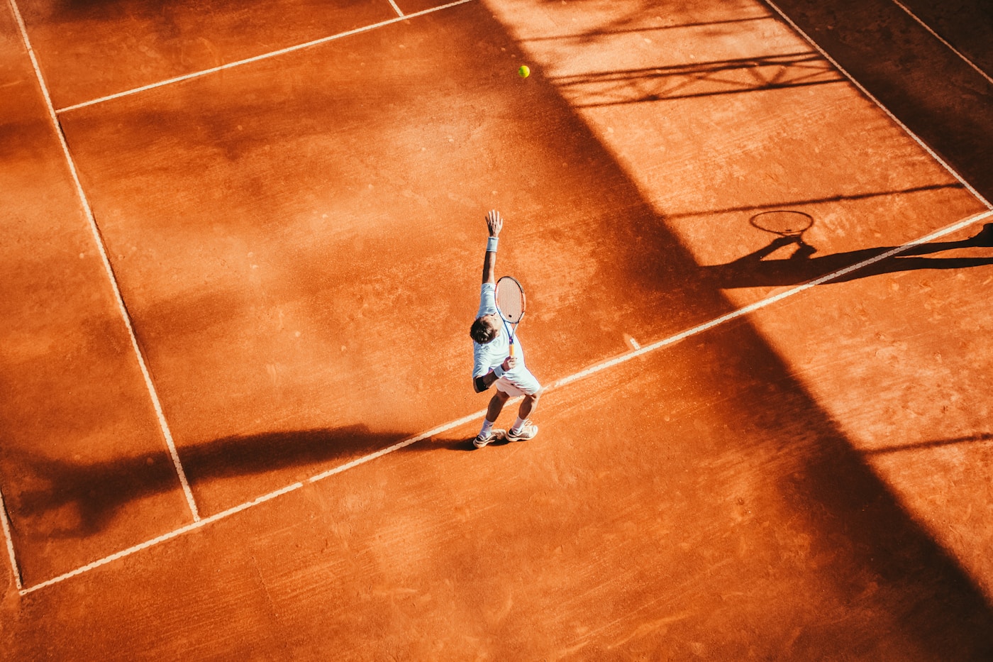 A tennis player serving on a sunlit court